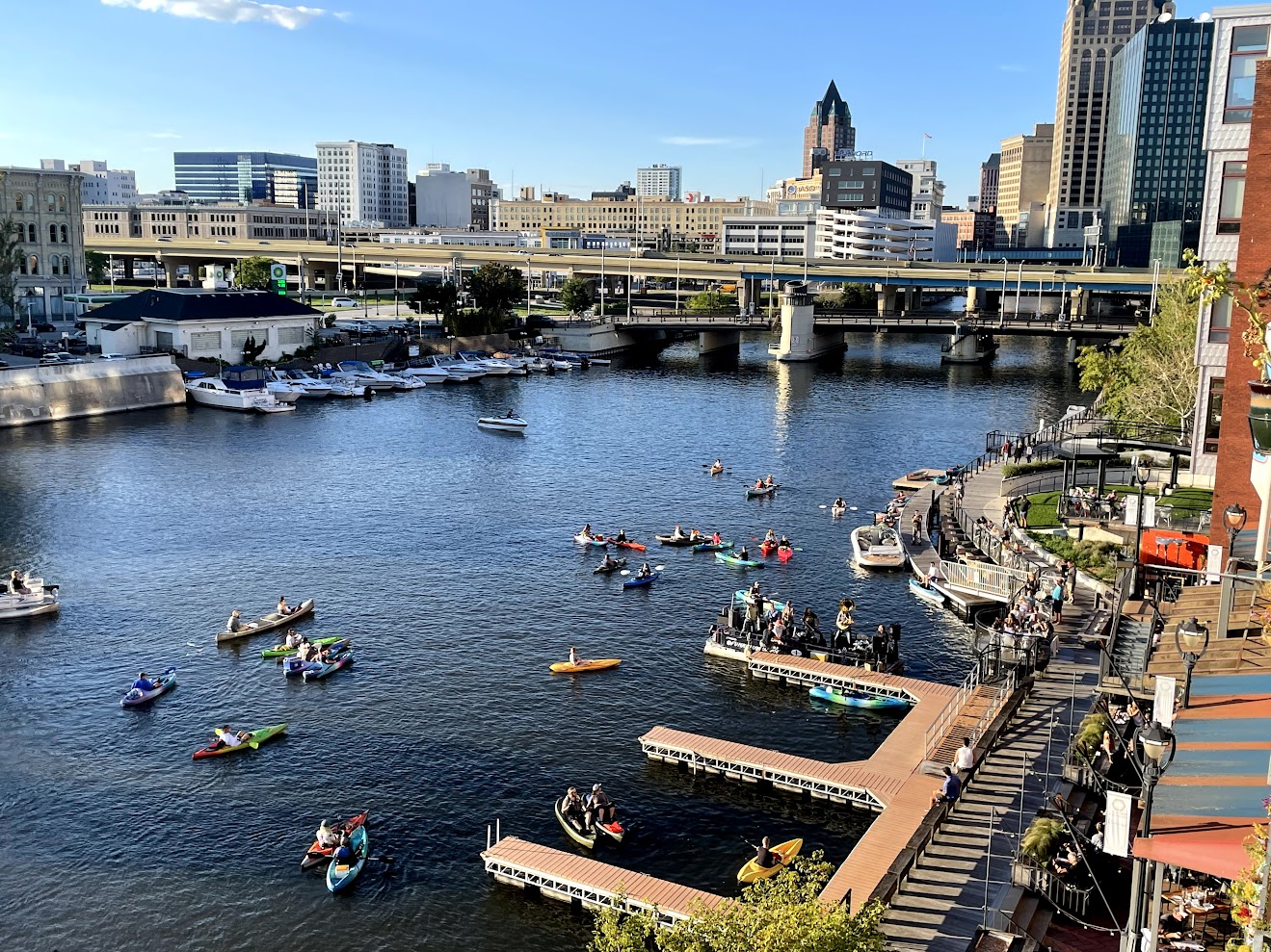 Lively summer scene on the Milwaukee River with kayakers, paddleboats, and the skyline