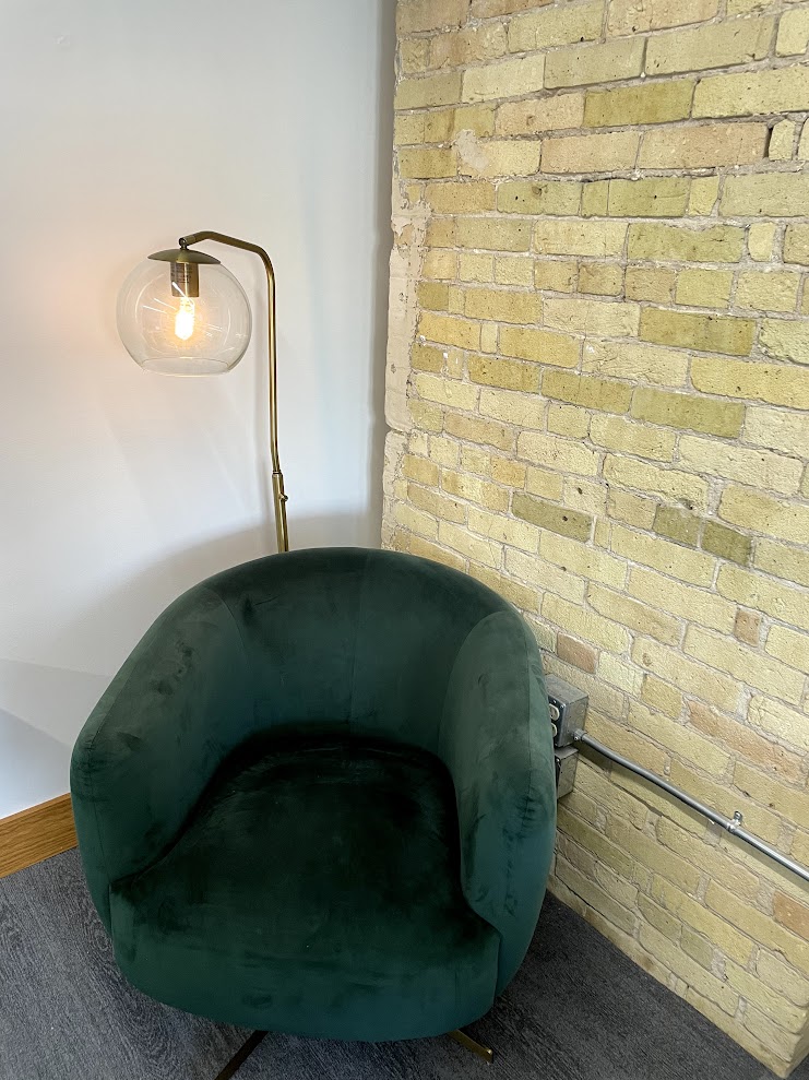 Single green velvet lounge chair with brass floor lamp against brick wall